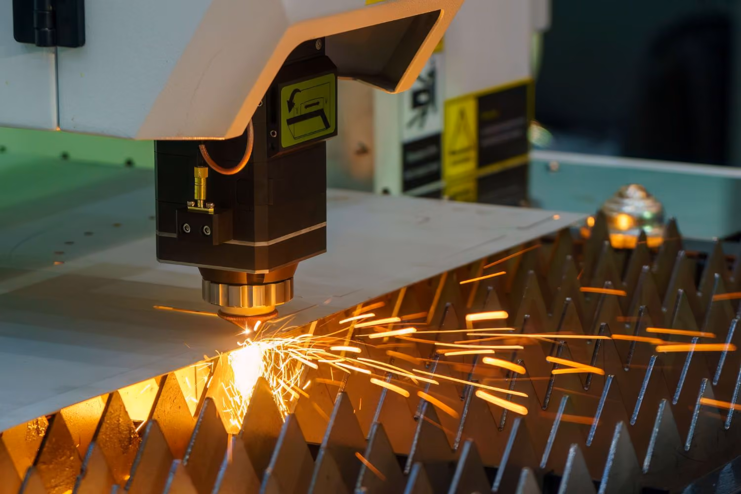 Laser cutting machine producing sparks while cutting a metal sheet on a industrial work surface.