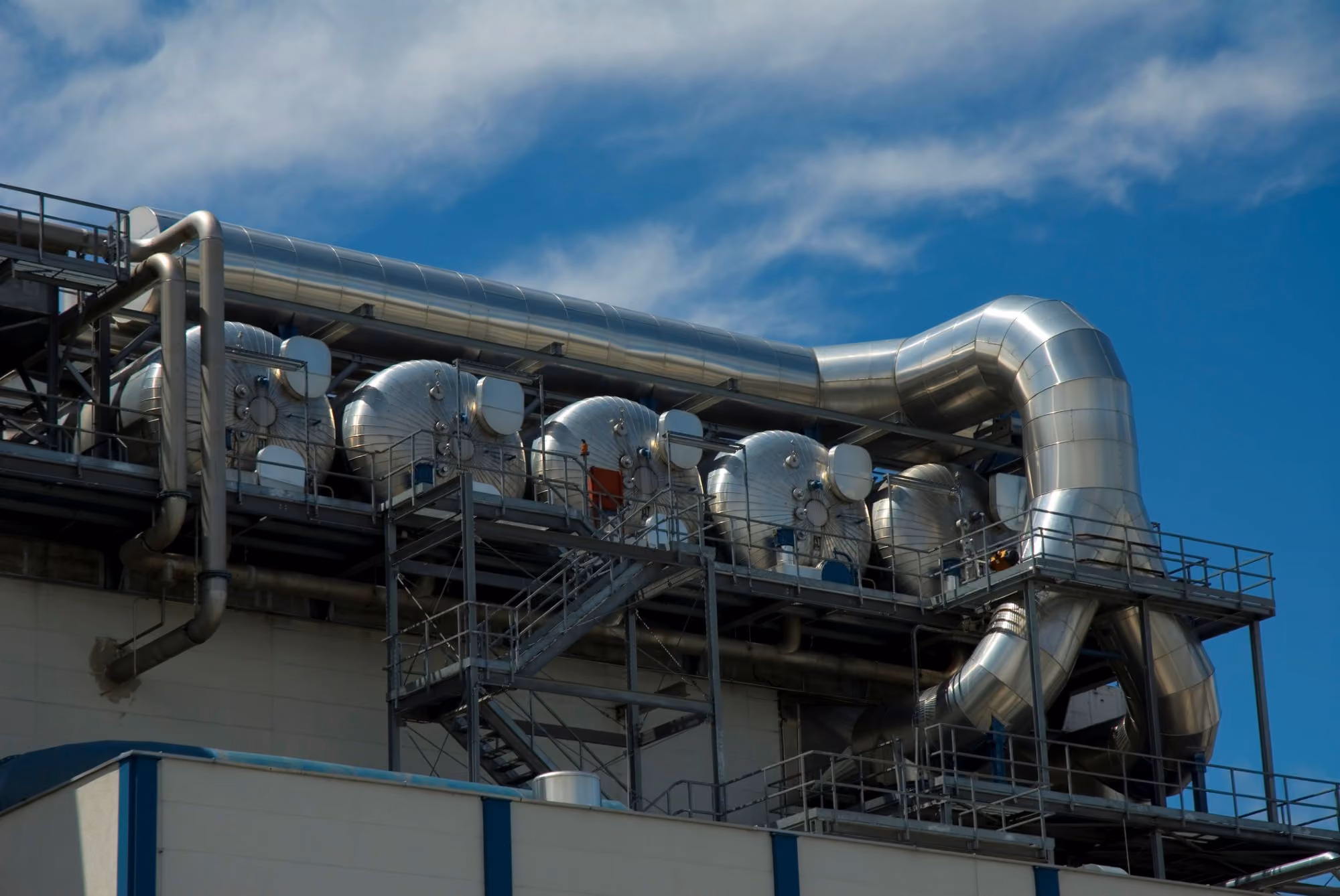Power plant with large shiny insulated metal pipes against a blue sky.