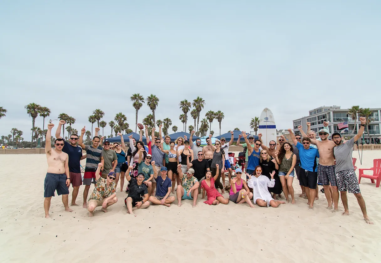 Group of people on beach raising fists, surrounded by palm trees, buildings, and beach chairs.