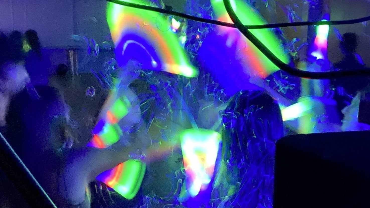 People interacting with colorful, glowing light ribbons in a dark environment, creating abstract neon patterns.