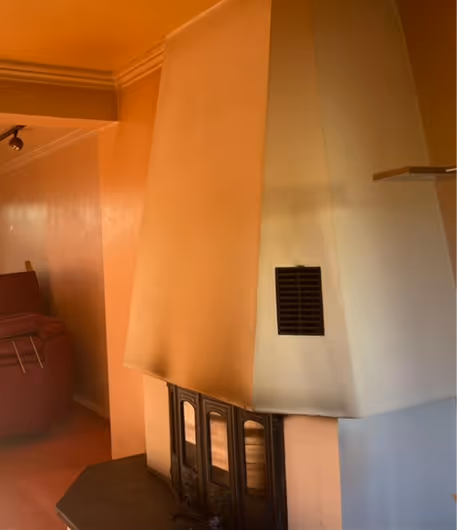 Moderner Kamin mit verglaster Tür und Kaminhaube in einem Wohnzimmer mit Sofa.