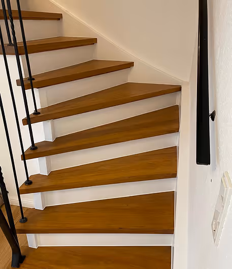 Holztreppe mit weißen Seitenwänden und schwarzem Geländer an der linken Seite in einem Innenraum.