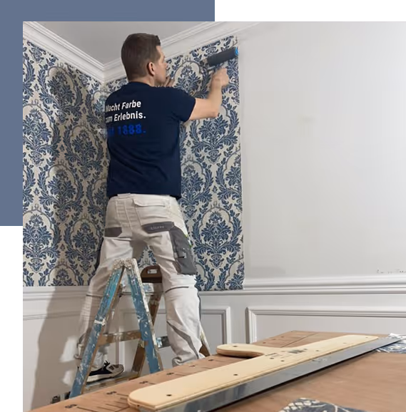 Mann steht auf einer Leiter und tapeziert eine Ecke mit blau-weiß gemustertem Tapetenmuster.