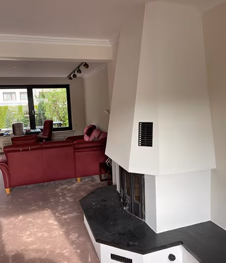 Wohnzimmer mit weißem Kamin und roten Sofas neben einem großen Fenster mit Blick auf Garten.
