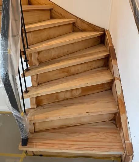 Holztreppe mit kurvigem Geländer und sichtbaren Gebrauchsspuren im Innenbereich.