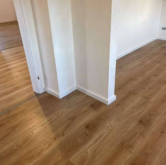 Ecke eines Raums mit hellbraunem Holzboden und weißen Wänden und Türrahmen.