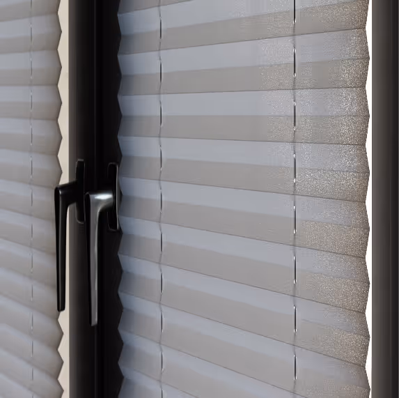 Geschlossene graue Faltjalousien mit zwei schwarzen Fenstergriffen an einem Fenster.