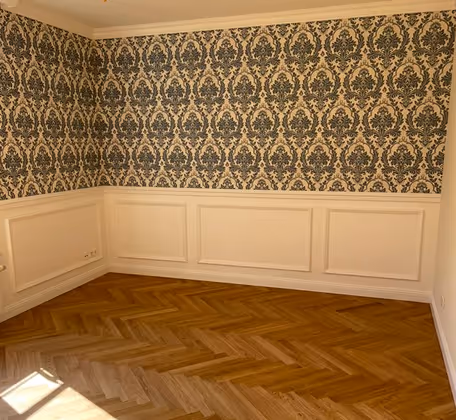 Leerer Raum mit Holzboden, dekorativer blauer Tapete und weißen Wandpaneelen.