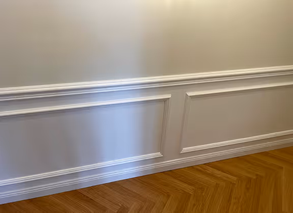 Weiß gestrichene Wand mit dekorativen Wandpaneelen und Holzparkettboden.