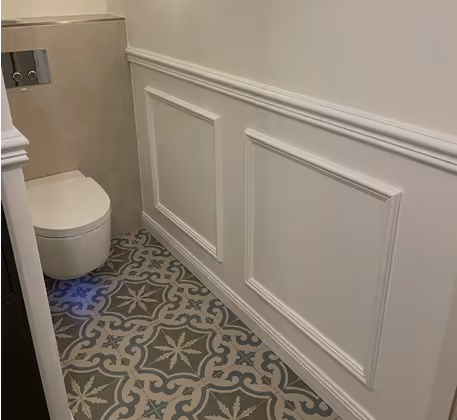 Kleines Badezimmer mit wandhängender Toilette, weißen Wandpaneelen und gemustertem Fliesenboden.