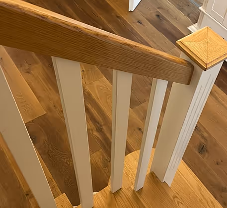Holztreppe mit weiß gestrichenen Geländerstäben und Holzhandlauf auf Holzboden.