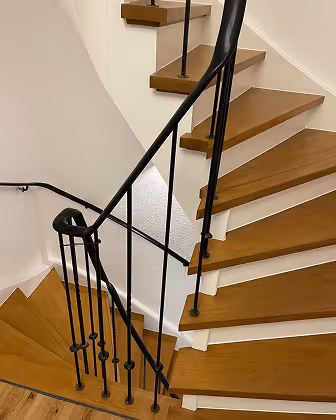 Holztreppe mit schwarzem Metallgeländer in einem weißen Innenraum.