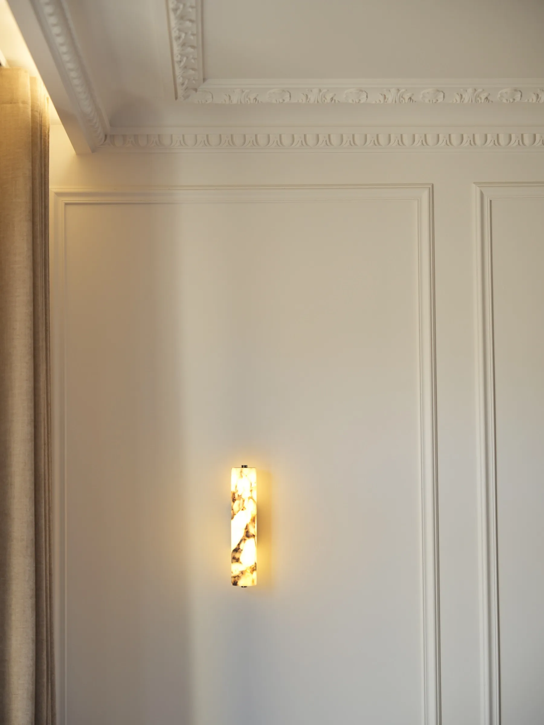 Mur en boiseries moulurées et corniche ornementée d'un appartement dijonnais, éclairé par une applique en albâtre