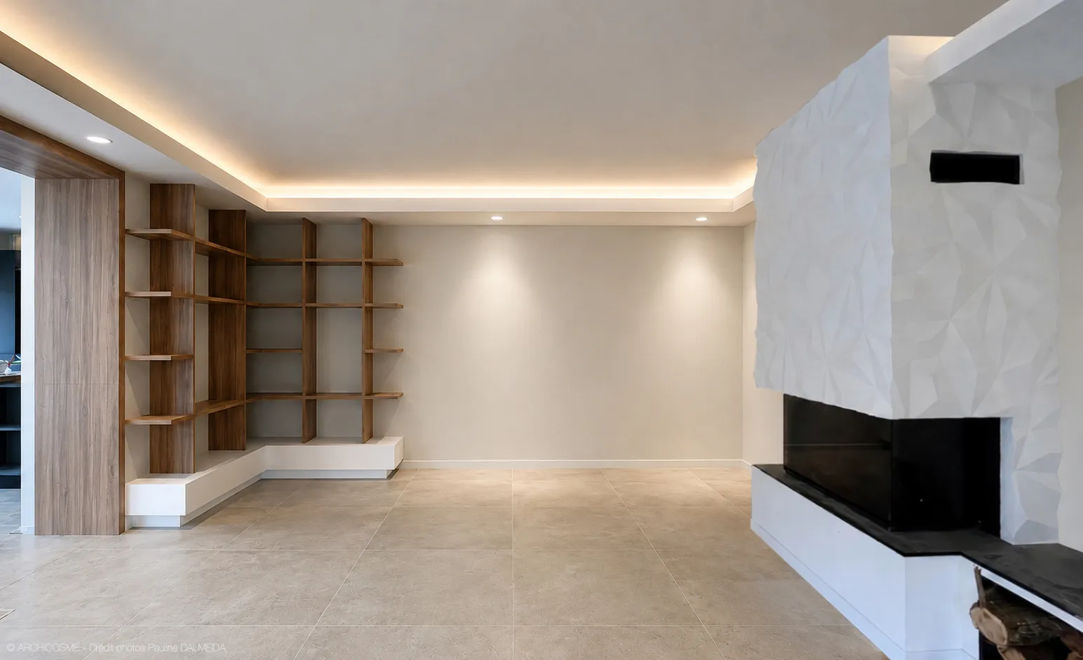 Séjour contemporain à faux plafond lumineux, étagères sur mesure et cheminée habillée d'un parement à facettes