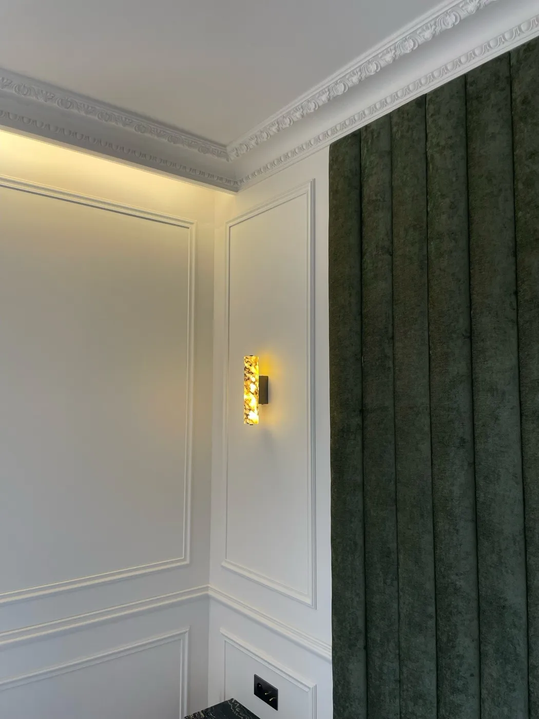 Angle de salon en boiseries moulurées et corniche ornementée, applique en albâtre et rideau de velours vert