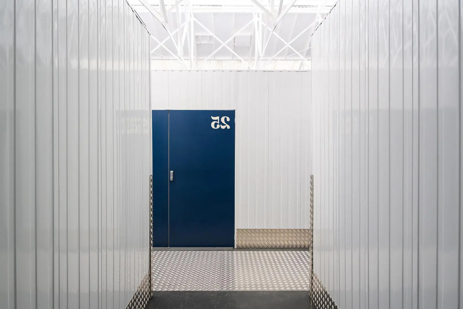 Hallway of white storage units leads to a blue door marked with white number 25.