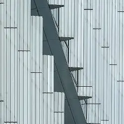 Gray staircase with metal railings on side of white corrugated metal building wall.