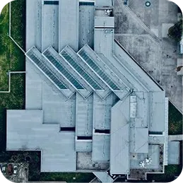 Aerial view of a modern building with angular, geometric roof structures and surrounding pavement and grass.