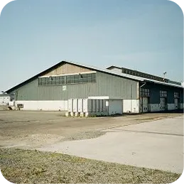 Large industrial warehouse building with gray exterior and clear sky above.