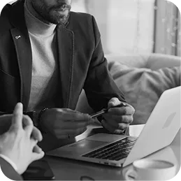 Man in a blazer holding a credit card near a laptop, sitting at a table with a coffee cup and phone.