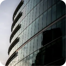 Curved glass facade of a modern building reflecting the sky and nearby structures.