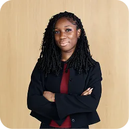 Confident woman with long curly hair wearing a black blazer and red top, arms crossed.