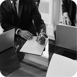 Two people in business attire working at a glass table with a laptop and documents.