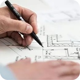 Hand holding a pen drawing on an architectural blueprint with detailed floor plan lines.