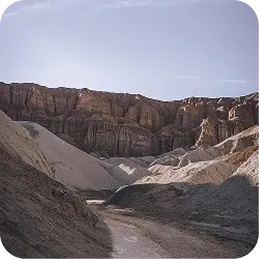 Dry desert canyon with rocky cliffs and a dirt path under a clear sky.