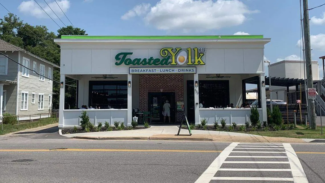 Exterior of Toasted Yolk Café with signage reading Breakfast, Lunch, Drinks under partly cloudy sky.