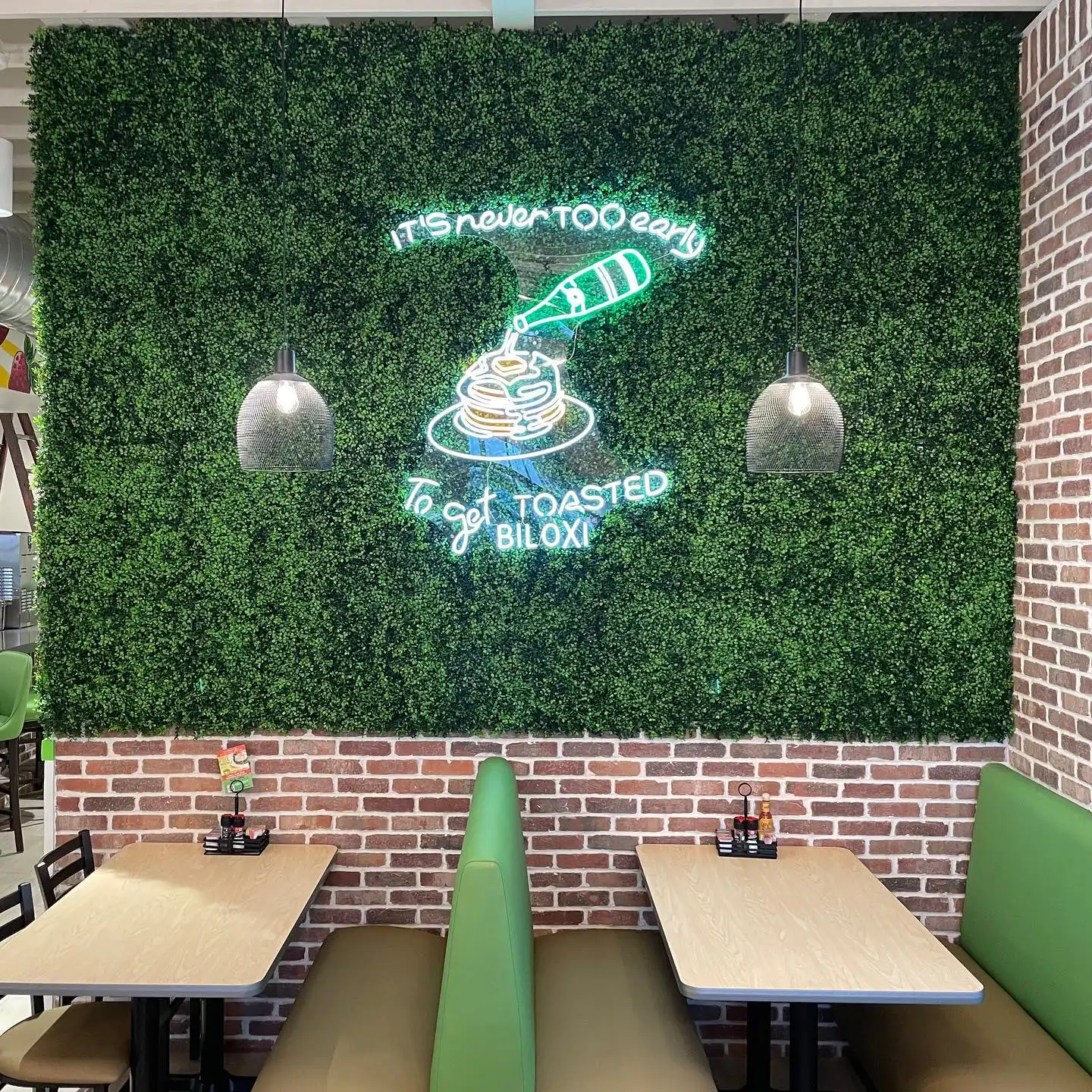 Restaurant booth seating with green cushions and a neon sign reading It’s never too early to get toasted Biloxi.