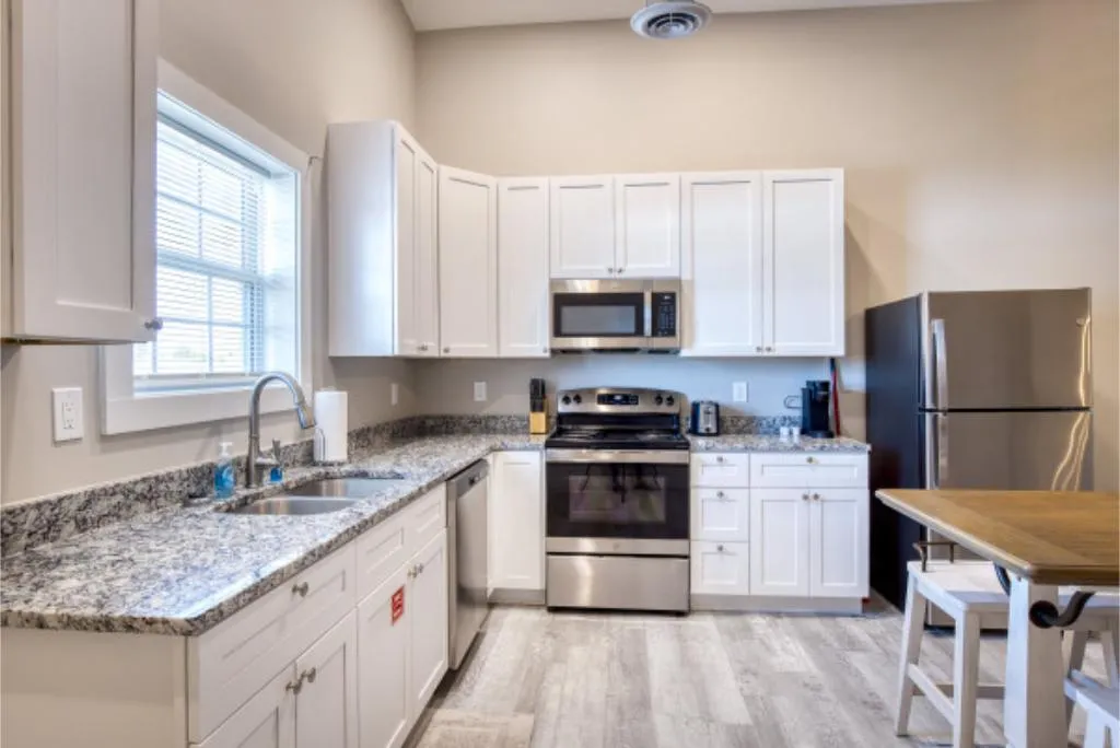 Modern kitchen with white cabinets, granite countertops, stainless steel appliances, and wooden dining table with chairs.