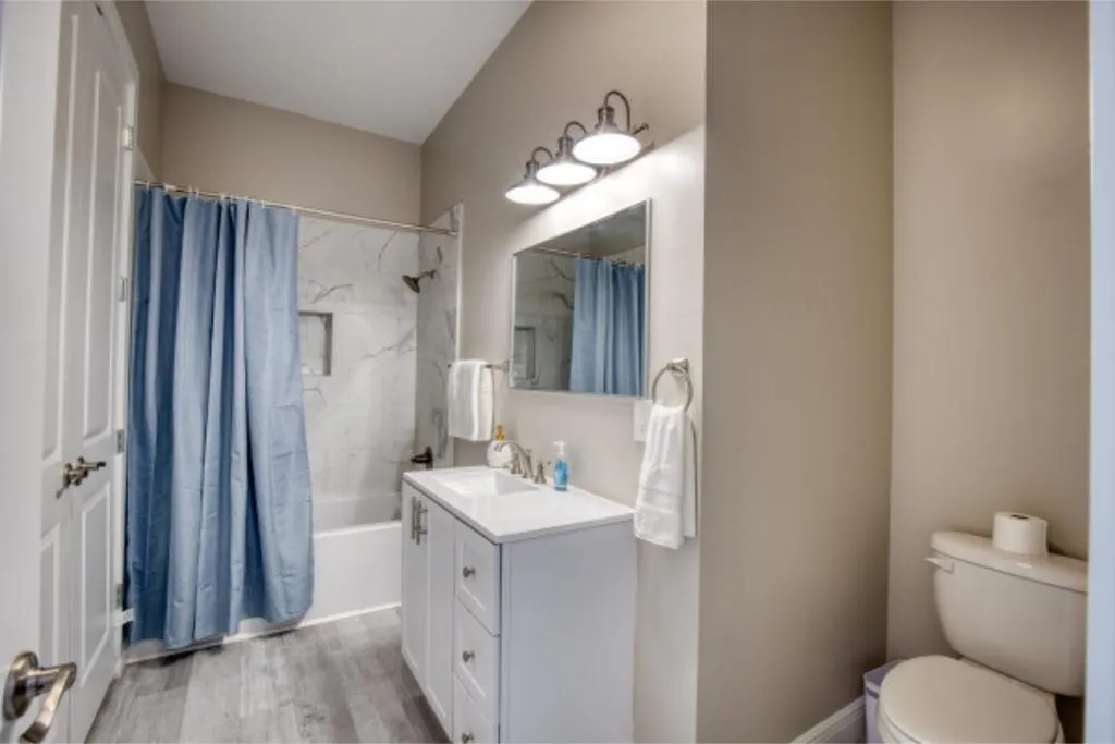 Modern bathroom with a white vanity, large mirror, blue shower curtain, and toilet with toilet paper.