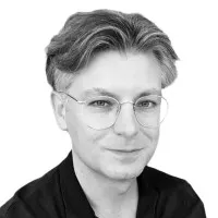 Porträt eines Mannes mit Brille, hellen Haaren und dunklem Hemd vor weißem Hintergrund.