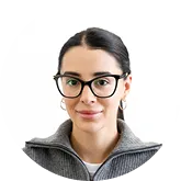 Portrait of a woman wearing black glasses and a gray sweater against a white background.