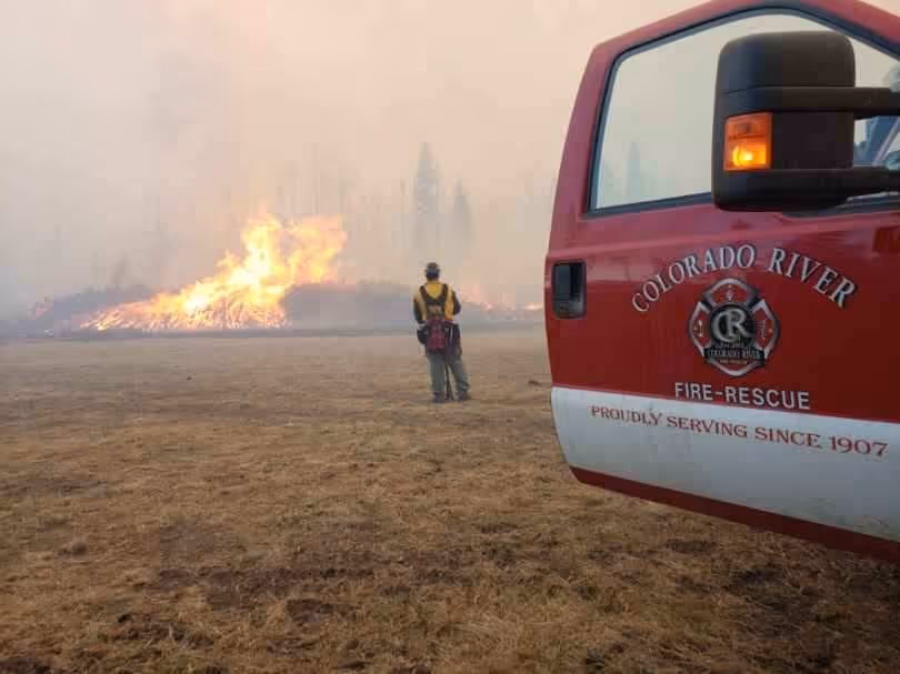Firefighter stands near a wildfire with a Colorado River Fire-Rescue truck in the foreground.