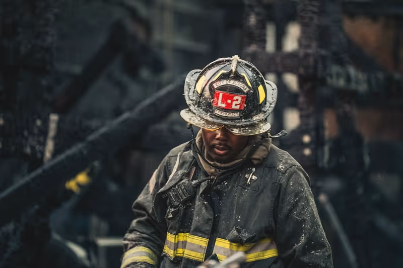 Firefighter in soot-covered gear and helmet labeled L-2 in a smoky, dark environment.