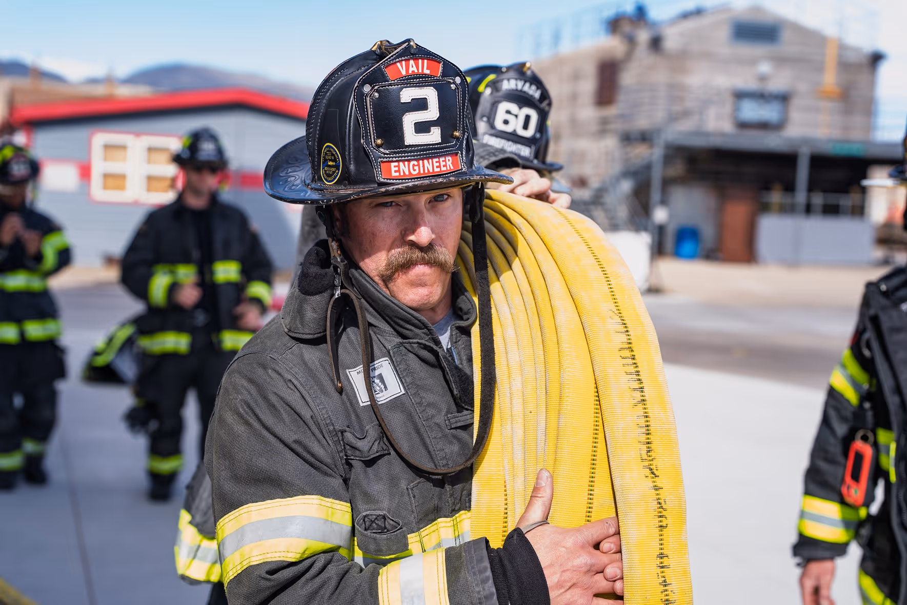 Firefighter wearing a helmet holding a coiled yellow fire hose on his shoulder.