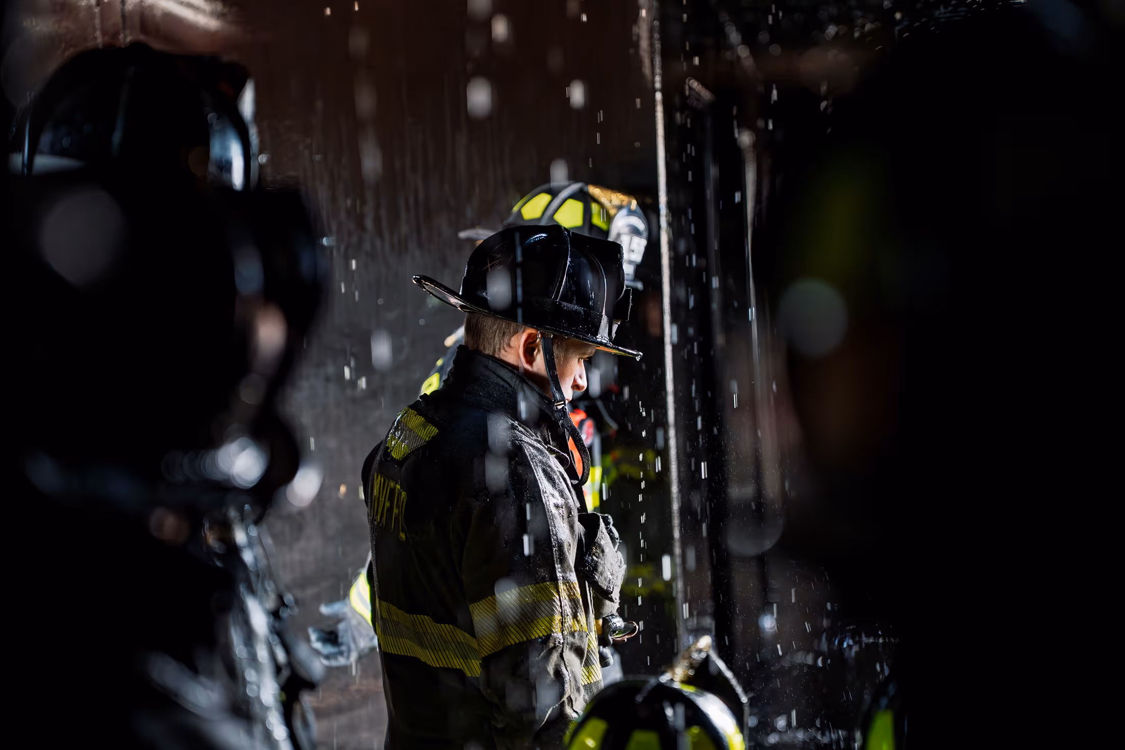 Firefighters in protective gear working amid falling water droplets in a dark environment.