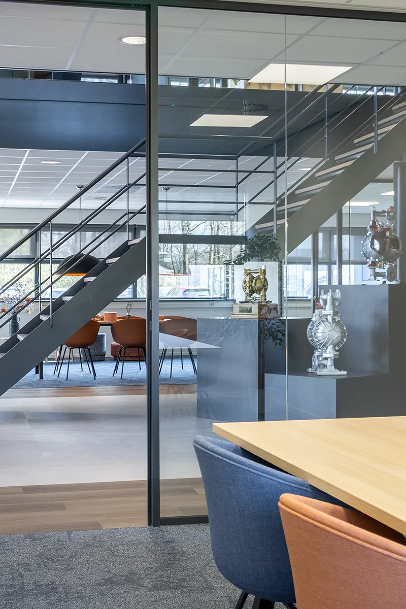 Doorkijk door glazen wand in kantoor Yamada Europe met uniforme plafondverlichting en open vide met trap
