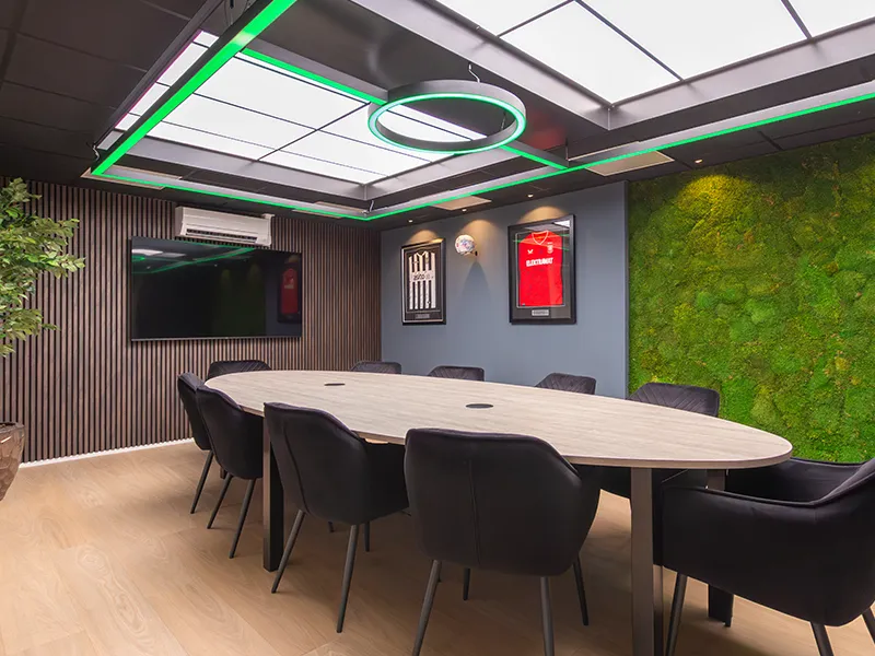 Vergaderruimte met groen verlichte LED-ring aan het plafond, lichtplafond en mosswand met ingelijste voetbalshirts