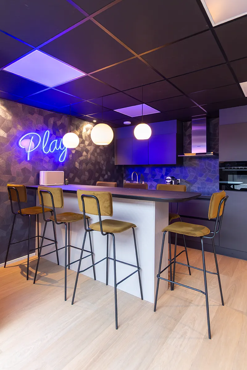Moderne kantoorkeuken met paars-blauwe LED-plafondverlichting, ronde hanglampen en blauw neonbord aan de wand