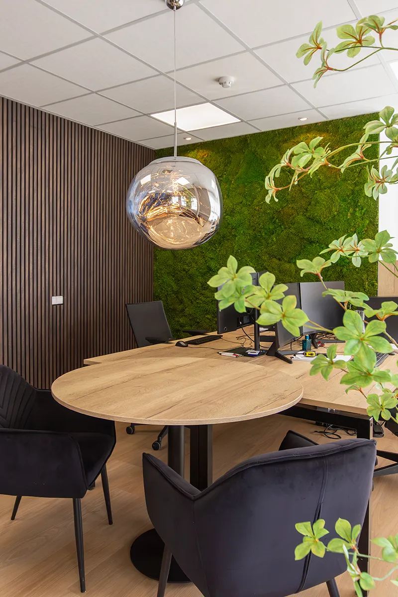 Werkplek in kantoor met spiegelende glazen bolhanglamp, donkere lamelwand en groene mosswand op de achtergrond