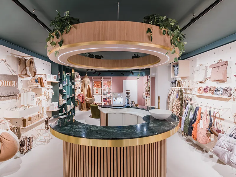 Overzicht van lifestyle winkel met centrale ronde balie, grote houten LED-ring aan plafond en zwarte railspots rondom