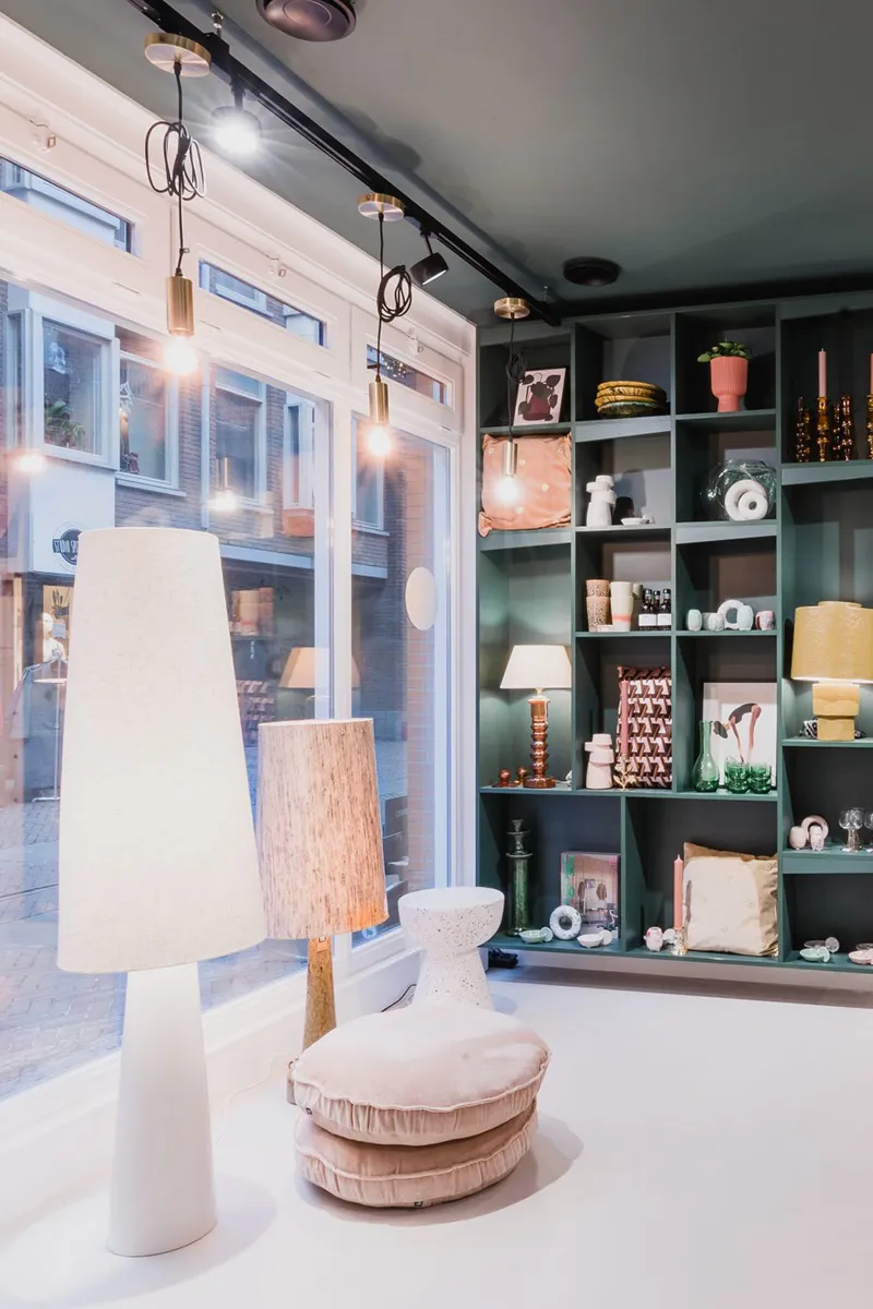 Lifestyle winkel met gouden hanglampen aan rail, staande lampen en groene wandkast vol woonaccessoires
