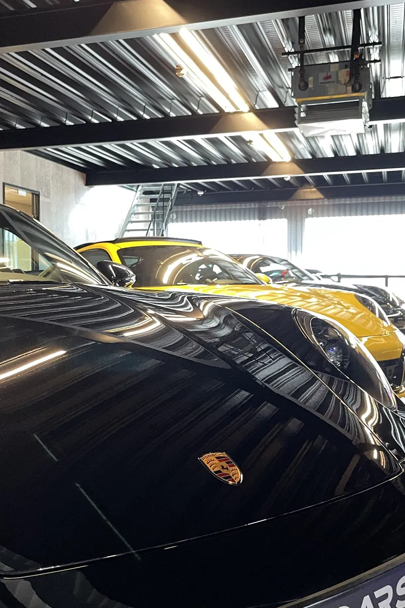 Detailopname van zwarte Porsche met reflectie van lineaire LED-verlichting in luxe autoshowroom