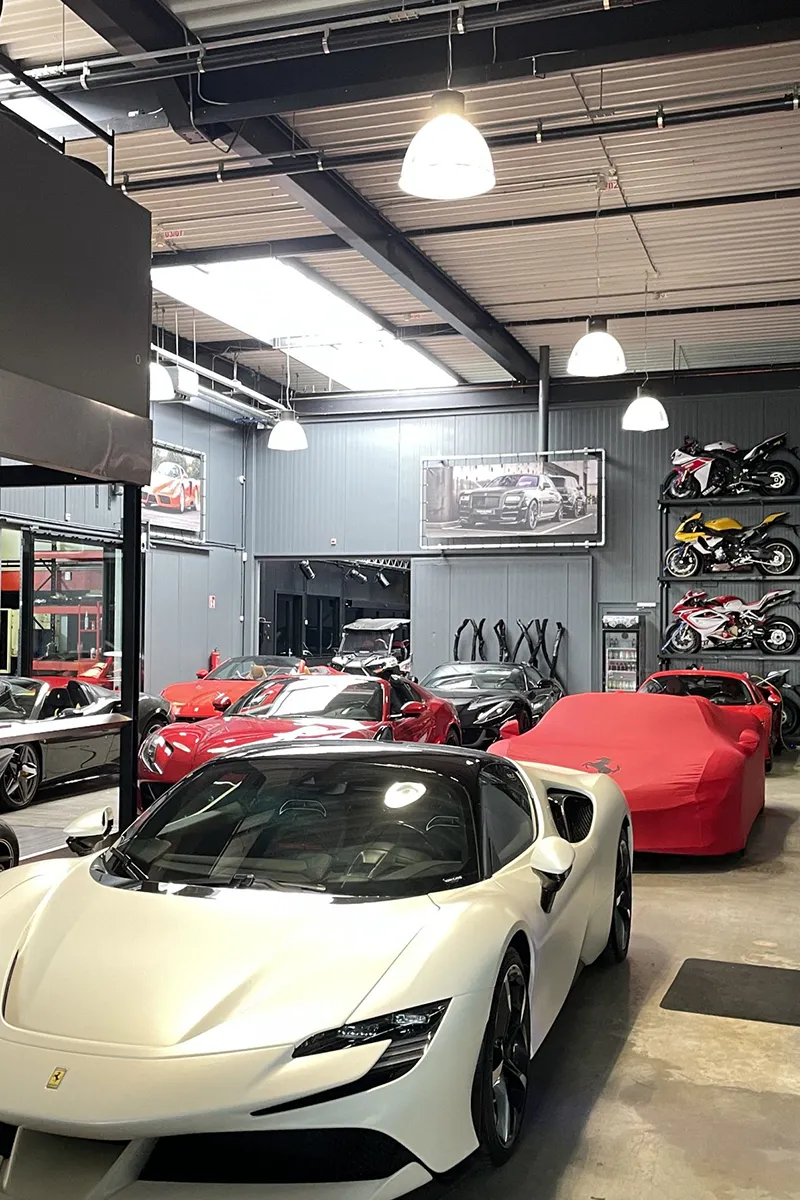 Supercar showroom met witte Ferrari, rode sportwagens en motoren op stellingen verlicht met koepelhanglampen en lineaire spots