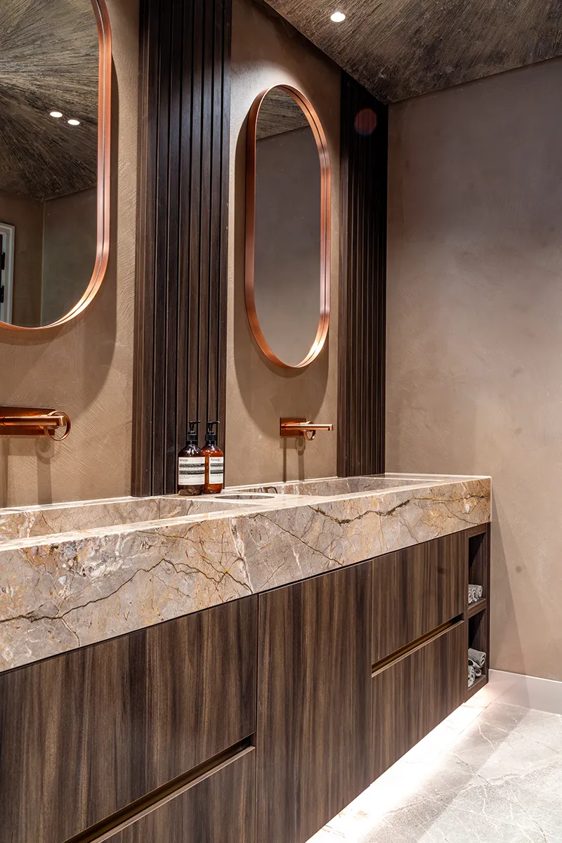 Luxe toiletruimte bij VDM Cars met koperen ovale spiegels, inbouwspots en marmeren wastafelblad verlicht door Halo Lighting