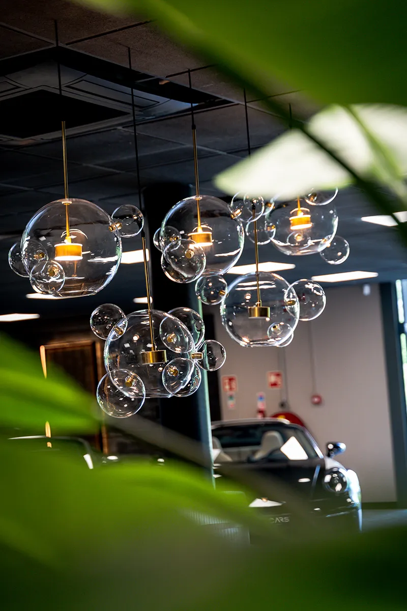 Glazen bubble hanglampen met gouden fitting boven supercar showroom van VDM Cars, gerealiseerd door Halo Lighting