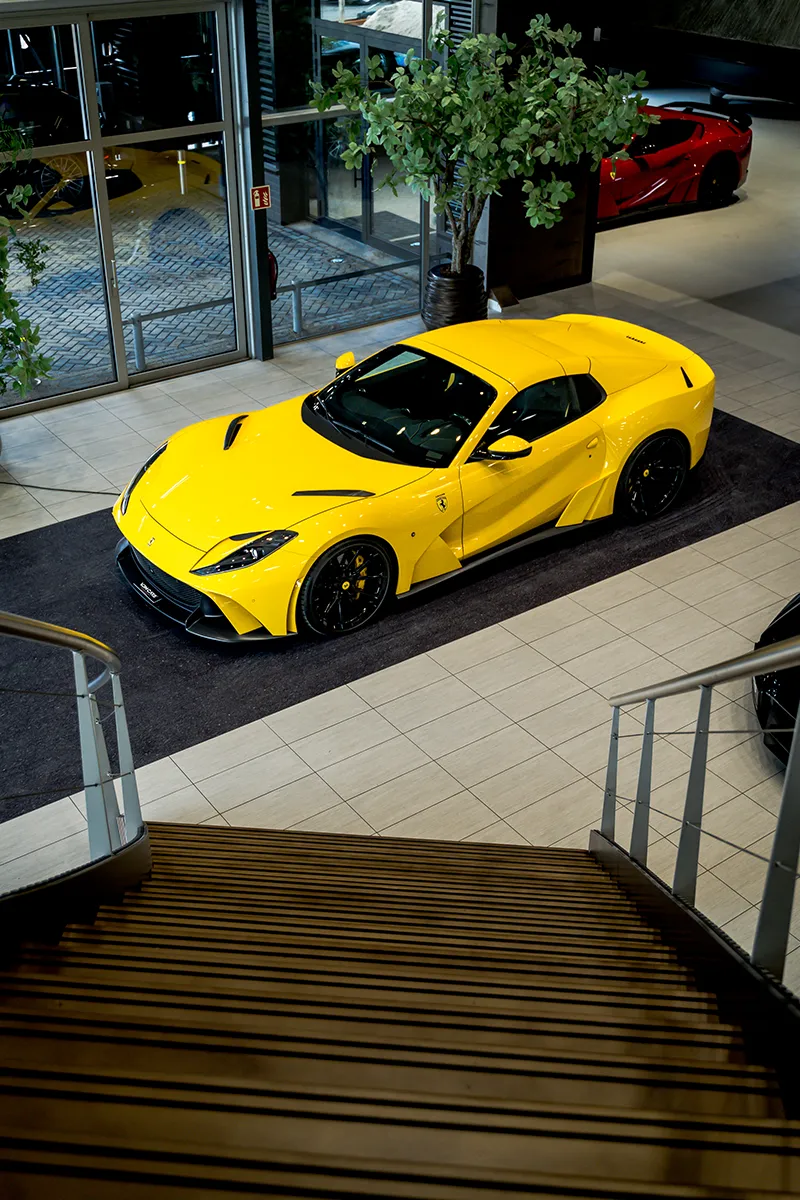 Bovenaanzicht van gele Ferrari in de verlichte showroom van VDM Cars met led-panelen aan het plafond
